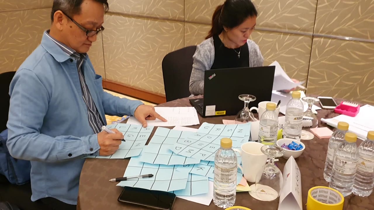 Two workshop participants prepare a paper learning game at a table.